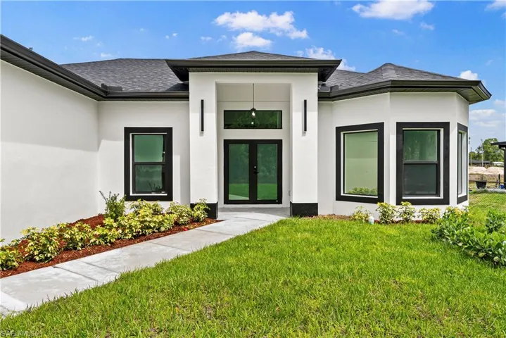 Doorway to property with french doors, stucco siding, a yard, and roof with shingles