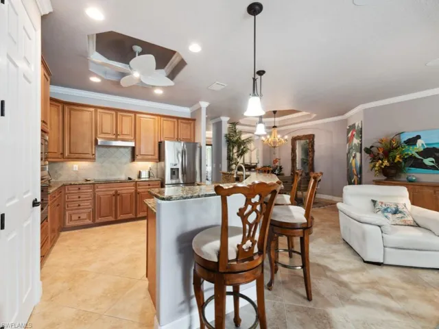 Kitchen featuring a kitchen breakfast bar, stainless steel refrigerator with ice dispenser, crown molding, stone countertops, and ceiling fan with notable chandelier