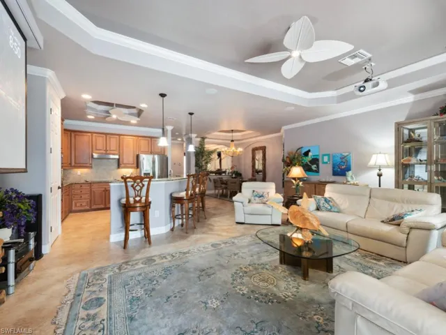 Living area with a tray ceiling, visible vents, ornamental molding, and ceiling fan with notable chandelier