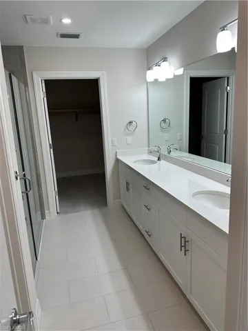 Bathroom featuring double vanity, a walk in closet, a stall shower, and light tile patterned floors