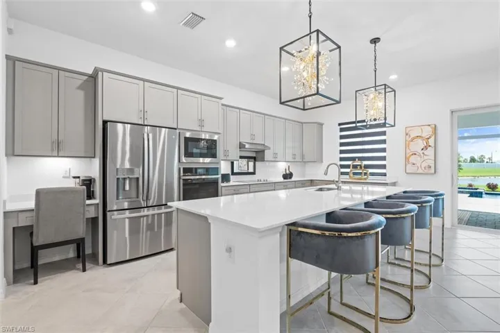 Kitchen with gray cabinetry, appliances with stainless steel finishes, a kitchen island with sink, decorative light fixtures, and sink