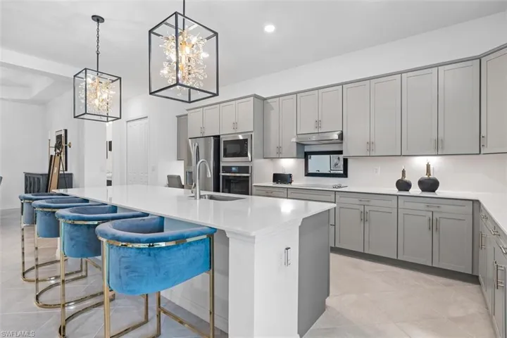 Kitchen featuring gray cabinetry, stainless steel appliances, a center island with sink, and a kitchen bar