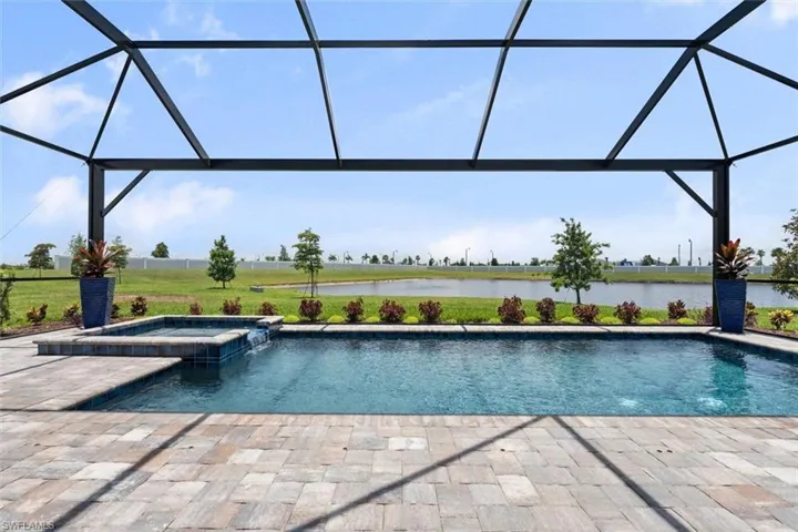 View of pool with an in ground hot tub, glass enclosure, a water view, and a patio