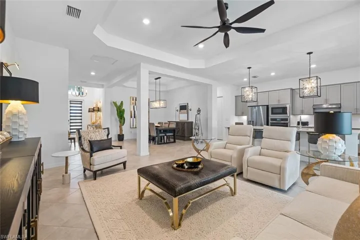 Living room with light tile floors, a raised ceiling, and ceiling fan with notable chandelier