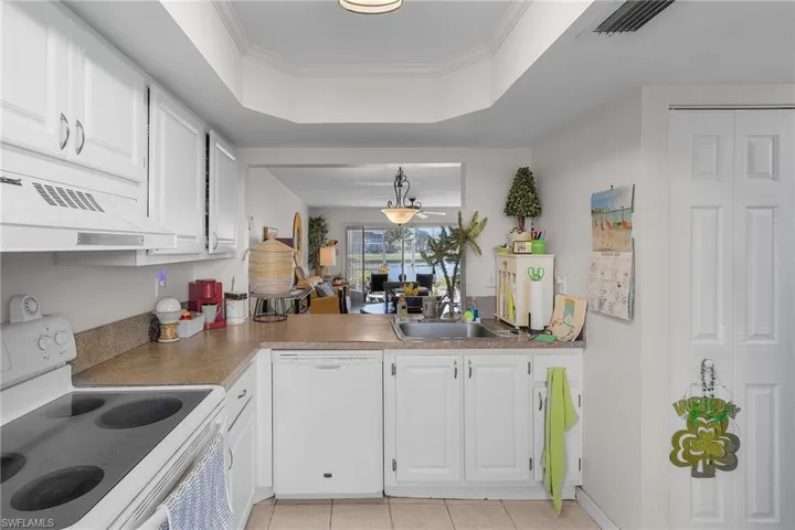 Kitchen with white cabinetry, white appliances, a tray ceiling, crown molding, and light tile patterned floors