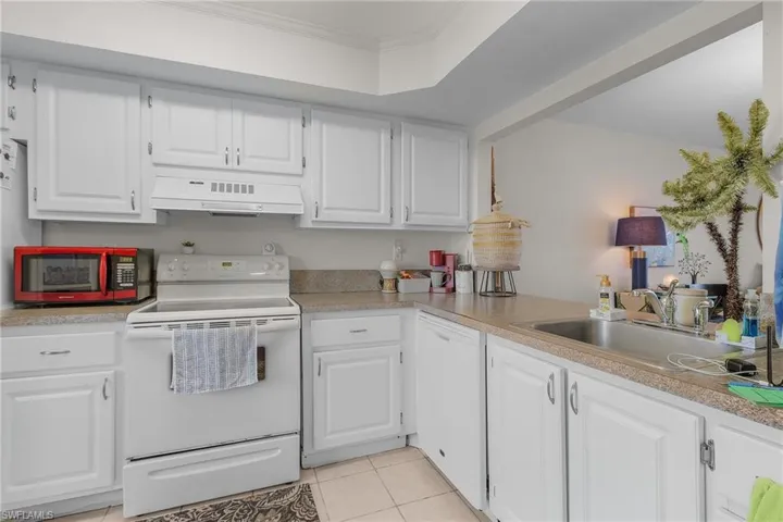 Kitchen with white appliances, white cabinets, light tile patterned floors, light countertops, and crown molding