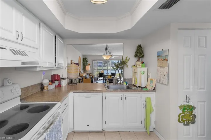 Kitchen with white cabinets, white appliances, a tray ceiling, crown molding, and under cabinet range hood