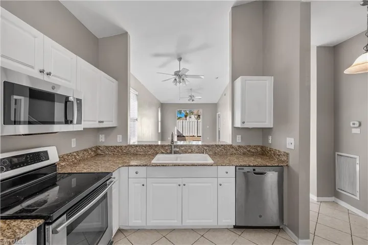 Kitchen featuring white cabinets, sink, ceiling fan, light tile patterned floors, and appliances with stainless steel finishes
