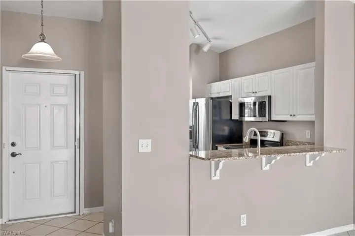 Kitchen with white cabinetry, kitchen peninsula, decorative light fixtures, a kitchen bar, and appliances with stainless steel finishes