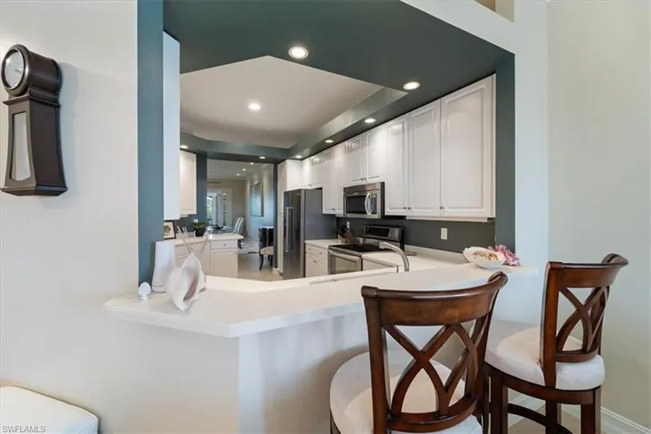 Kitchen featuring white cabinets, a breakfast bar area, stainless steel appliances, light countertops, and recessed lighting