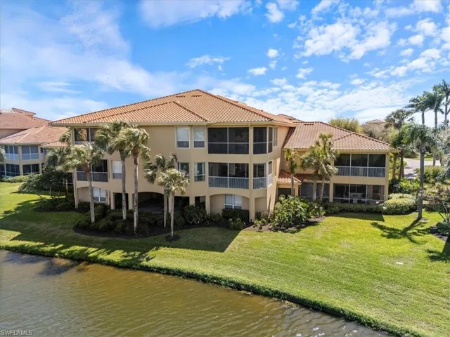 Back of property featuring a water view, stucco siding, a lawn, and a tiled roof