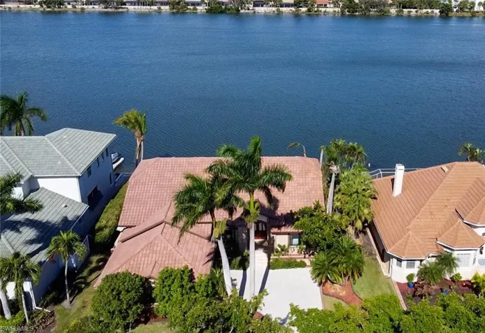 Waterfront property featuring a tile roof, mature palm trees, a concrete driveway, and established landscaping