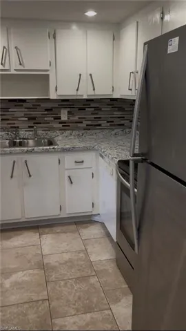 Kitchen with appliances with stainless steel finishes, white cabinets, backsplash, and light tile patterned floors