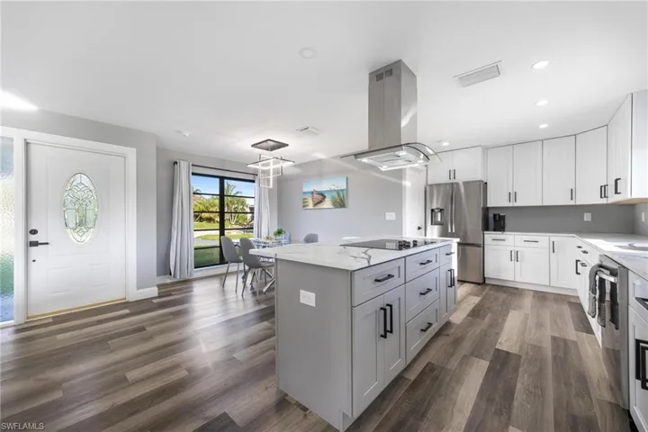 Kitchen featuring island range hood, dark wood-type flooring, stainless steel fridge with ice dispenser, and black electric cooktop