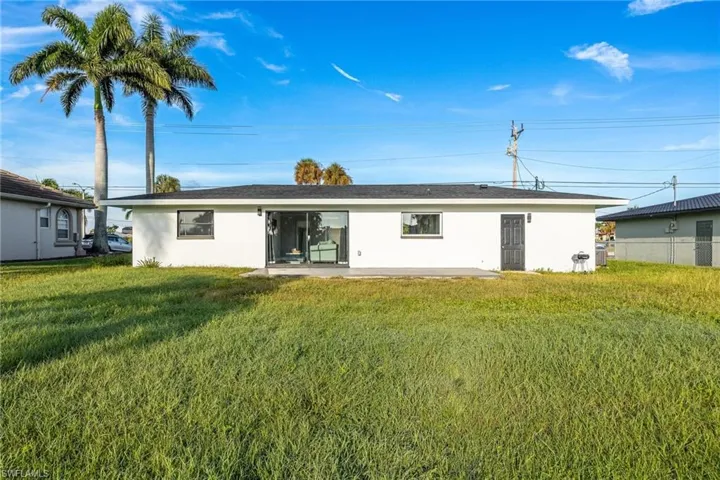 Rear view of property featuring stucco siding, a yard, and fence