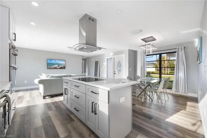 Kitchen with wood finished floors, a center island, black electric stovetop, and island range hood