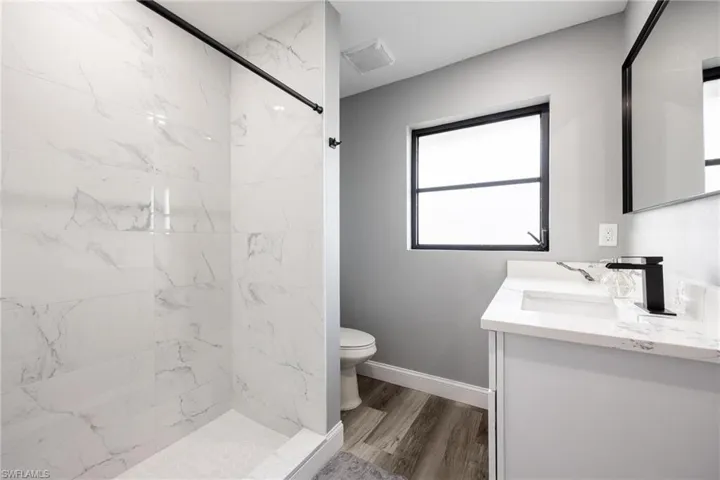 Bathroom featuring vanity, wood finished floors, baseboards, tiled shower, and toilet