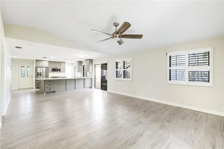 Living/dining room area with kitchen in the background, custom plantation shutters throughout ALL windows, wood grain pattern ceramic tile throughout the entire property, slider to side private patio and garden area!