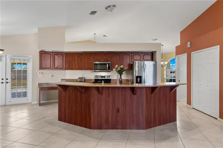 Kitchen with stainless steel appliances, a chandelier, light tile flooring, and lofted ceiling