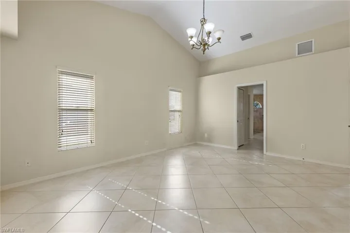 Tiled empty room with high vaulted ceiling, plenty of natural light, and an inviting chandelier