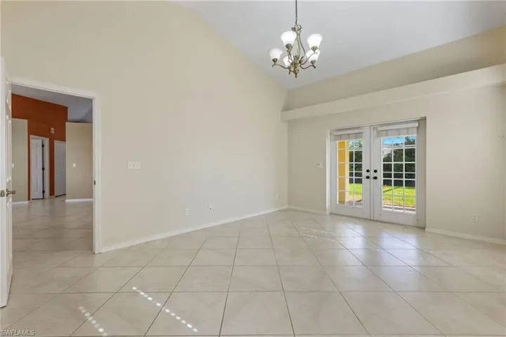 Unfurnished room with high vaulted ceiling, light tile floors, an inviting chandelier, and french doors