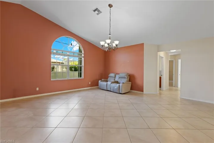 Unfurnished room featuring an inviting chandelier, light tile flooring, and vaulted ceiling