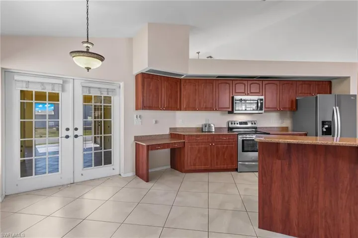 Kitchen featuring decorative light fixtures, light tile flooring, stainless steel appliances, high vaulted ceiling, and french doors