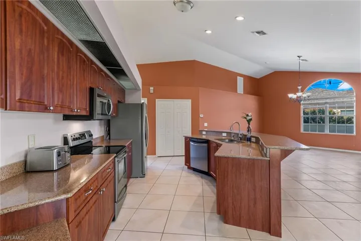 Kitchen with a chandelier, stainless steel appliances, a kitchen island with sink, sink, and lofted ceiling