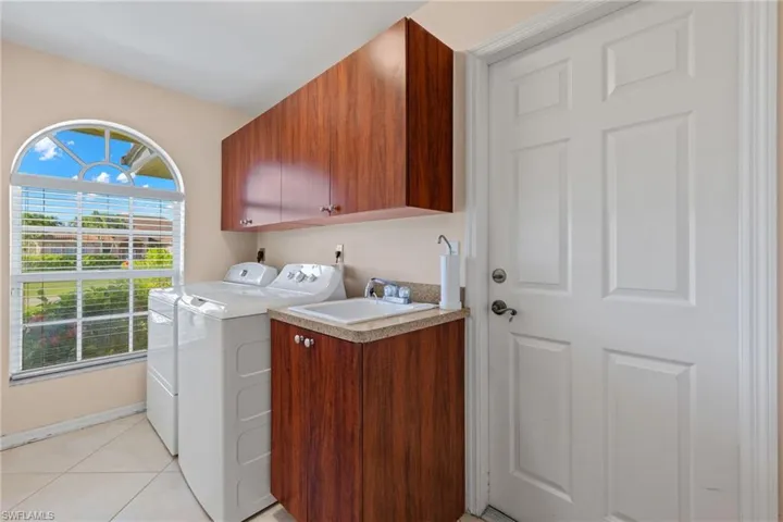 Clothes washing area with washer and dryer, cabinets, sink, and light tile floors