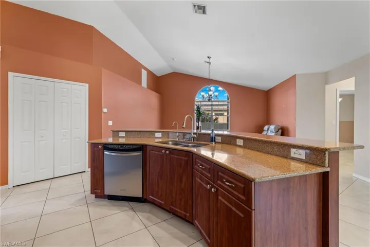 Kitchen featuring light stone countertops, sink, light tile flooring, dishwasher, and vaulted ceiling