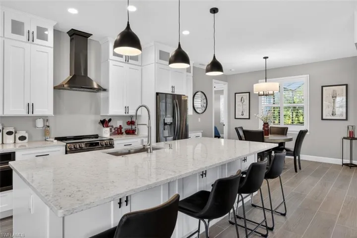 Kitchen with wood tiled floors, light stone countertops, pendant lighting, white cabinetry, and wall chimney exhaust hood