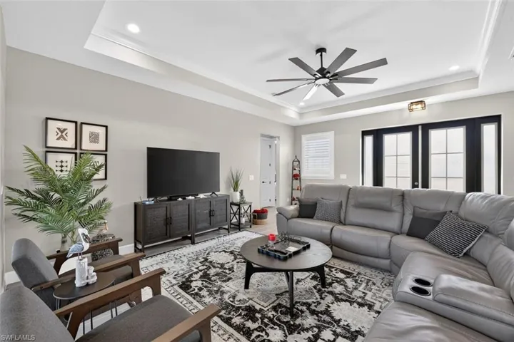 Living area featuring a raised ceiling, ornamental molding, ceiling fan, recessed lighting, and french doors