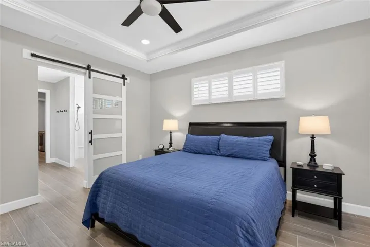 Bedroom with wood tiled floors, a barn door, ceiling fan, connected bathroom, and ornamental molding