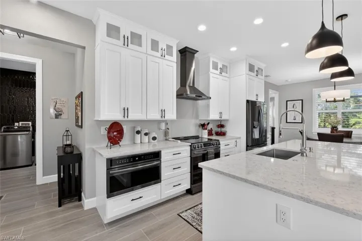 Kitchen with decorative light fixtures, light stone countertops, stainless steel appliances, washer / clothes dryer, and wall chimney exhaust hood