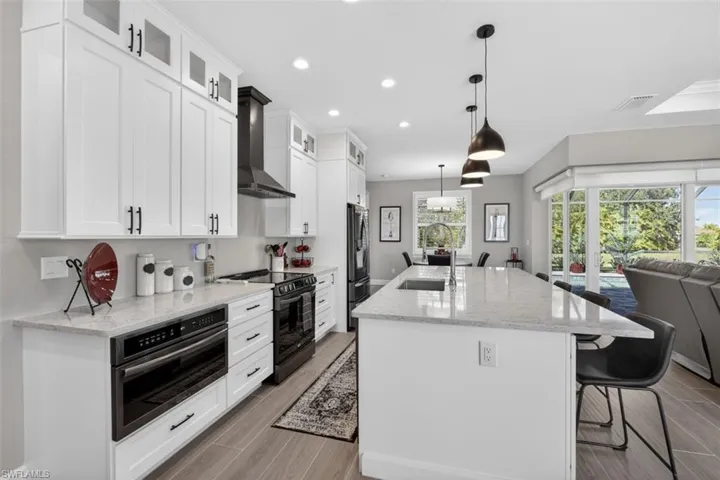 Kitchen with a breakfast bar area, light stone counters, recessed lighting, stainless steel appliances, and a kitchen island with sink
