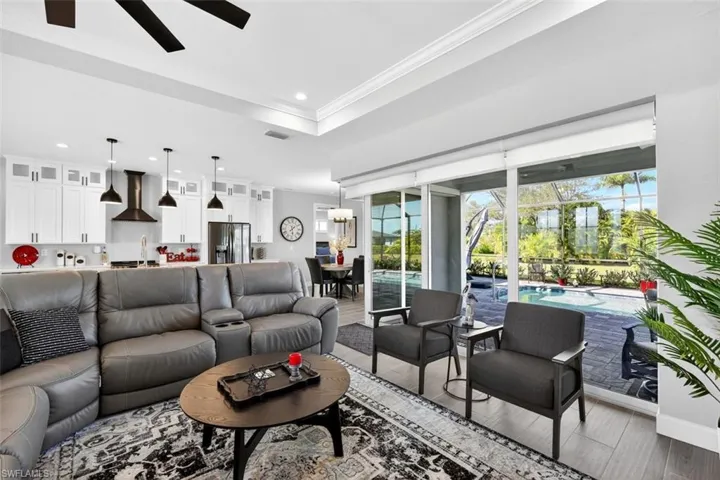Living area featuring light wood-style floors, plenty of natural light, a ceiling fan, recessed lighting, and a tray ceiling