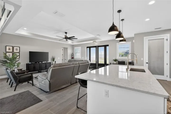 Kitchen with light stone counters, wood tiled floors, decorative light fixtures, an island with sink, and a breakfast bar area