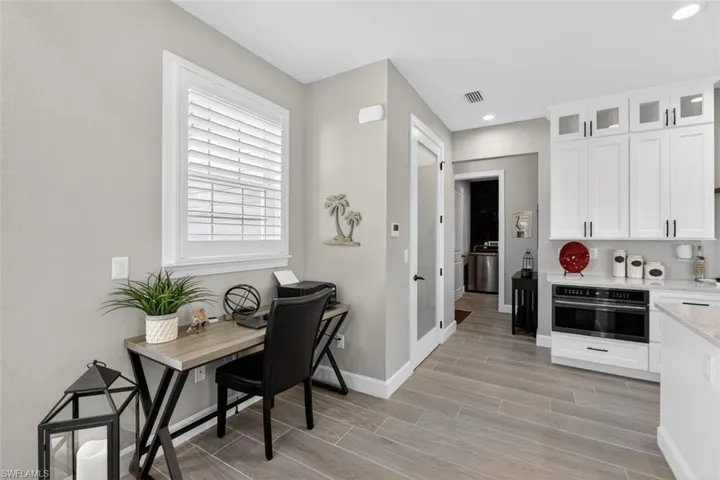 Kitchen featuring white cabinetry, black oven, glass insert cabinets, light stone countertops, and wood tiled floors