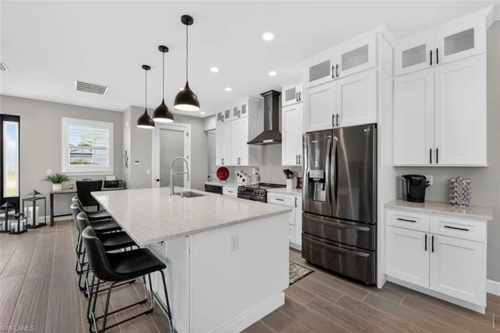 Kitchen with appliances with stainless steel finishes, glass insert cabinets, light stone countertops, a kitchen island with sink, and a breakfast bar