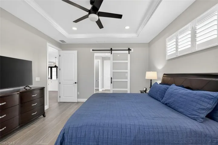 Bedroom with a barn door, wood finish floors, a ceiling fan, recessed lighting, and crown molding