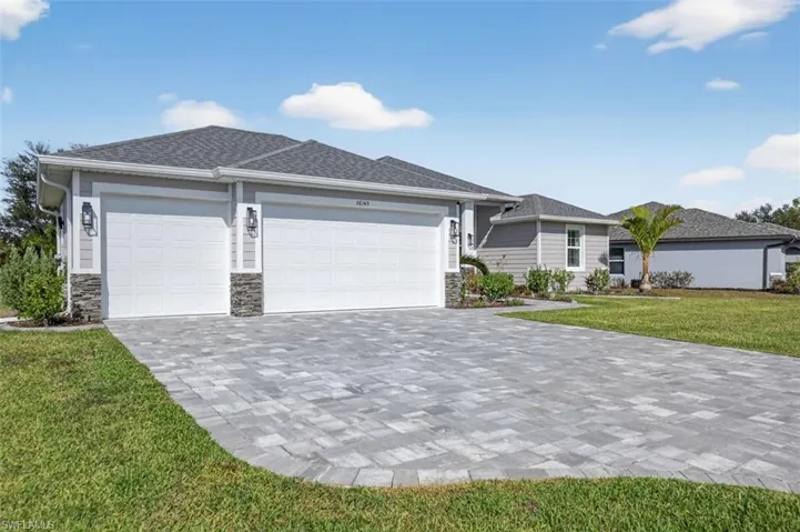 View of front of house featuring a front yard, stone siding, an attached garage, decorative driveway, and a shingled roof