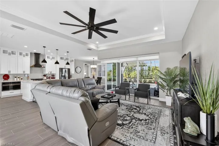 Living room with wood finish floors, a ceiling fan, a raised ceiling, ornamental molding, and recessed lighting