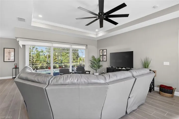 Living area featuring wood finish floors, a tray ceiling, ceiling fan, ornamental molding, and recessed lighting