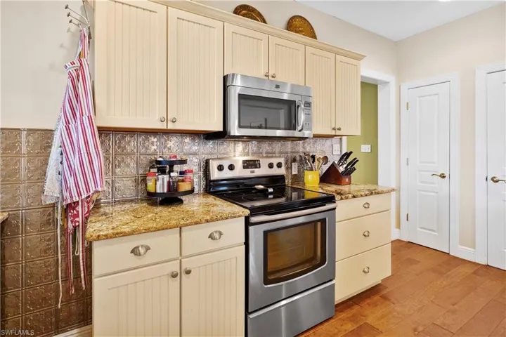Kitchen featuring cream cabinetry, stainless steel appliances, light wood-type flooring, light stone counters, and backsplash