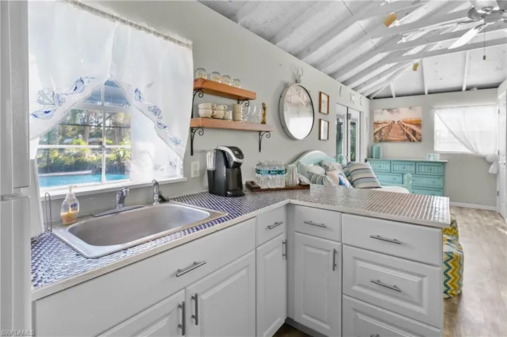 Pool house kitchen / bar featuring sink, white cabinets, lofted ceiling, ceiling fan, and kitchen peninsula