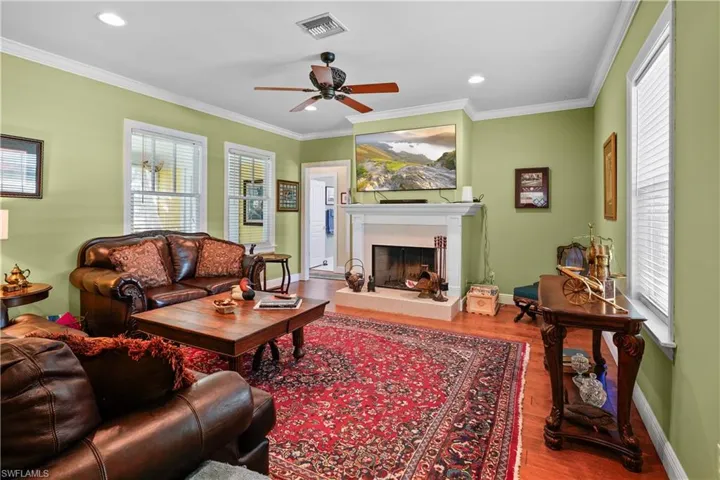 Living room featuring a tiled fireplace, hardwood / wood-style floors, a healthy amount of sunlight, and crown molding