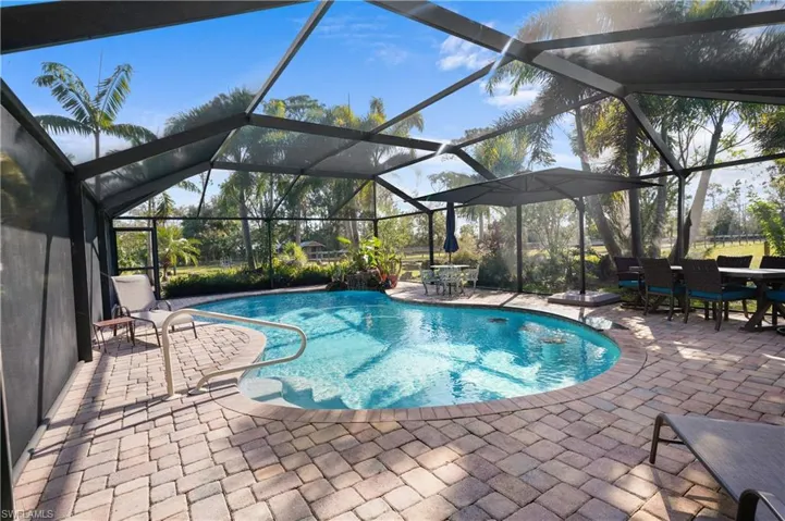 View of swimming pool water with fall with large paver deck and built in pool bar area with in pool stools and granite counter top.