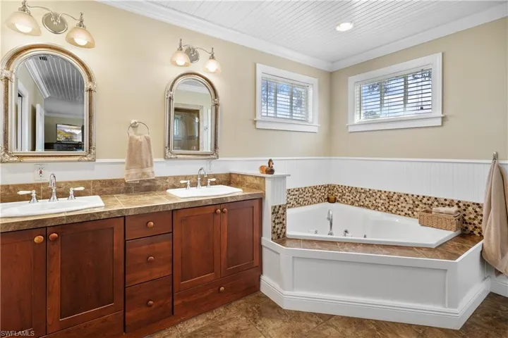 Owner's suite bathroom featuring double vanity, a tub to relax in, and plank ceiling and crown molding. The warm country feel flows through the home.