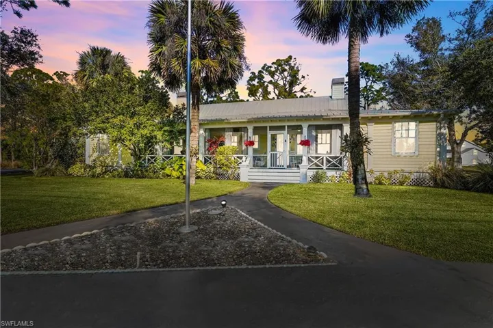 View of front of house featuring a huge screen porch, new flag pole and mature landscaping. Orchid lovers dream, large orchids on each palm as you enter the home!