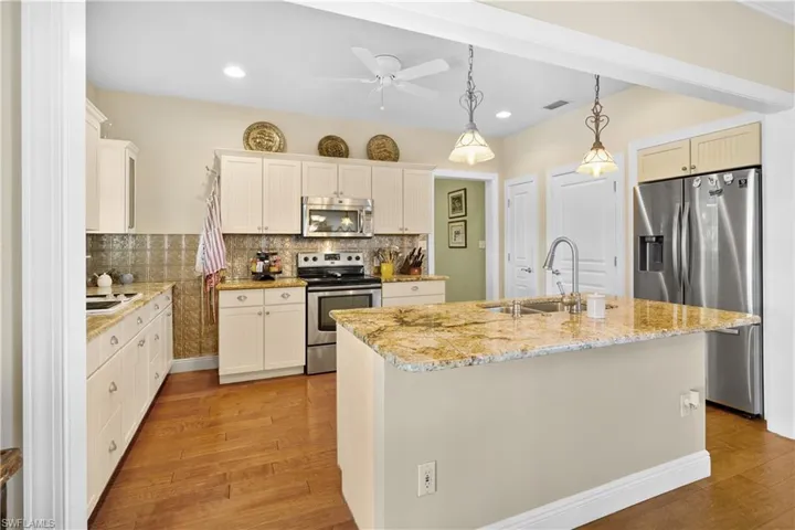 Country kitchen is perfect for the ranchette. It features decorative backsplash, a kitchen island with sink, pendant lighting, and appliances with stainless steel finishes.